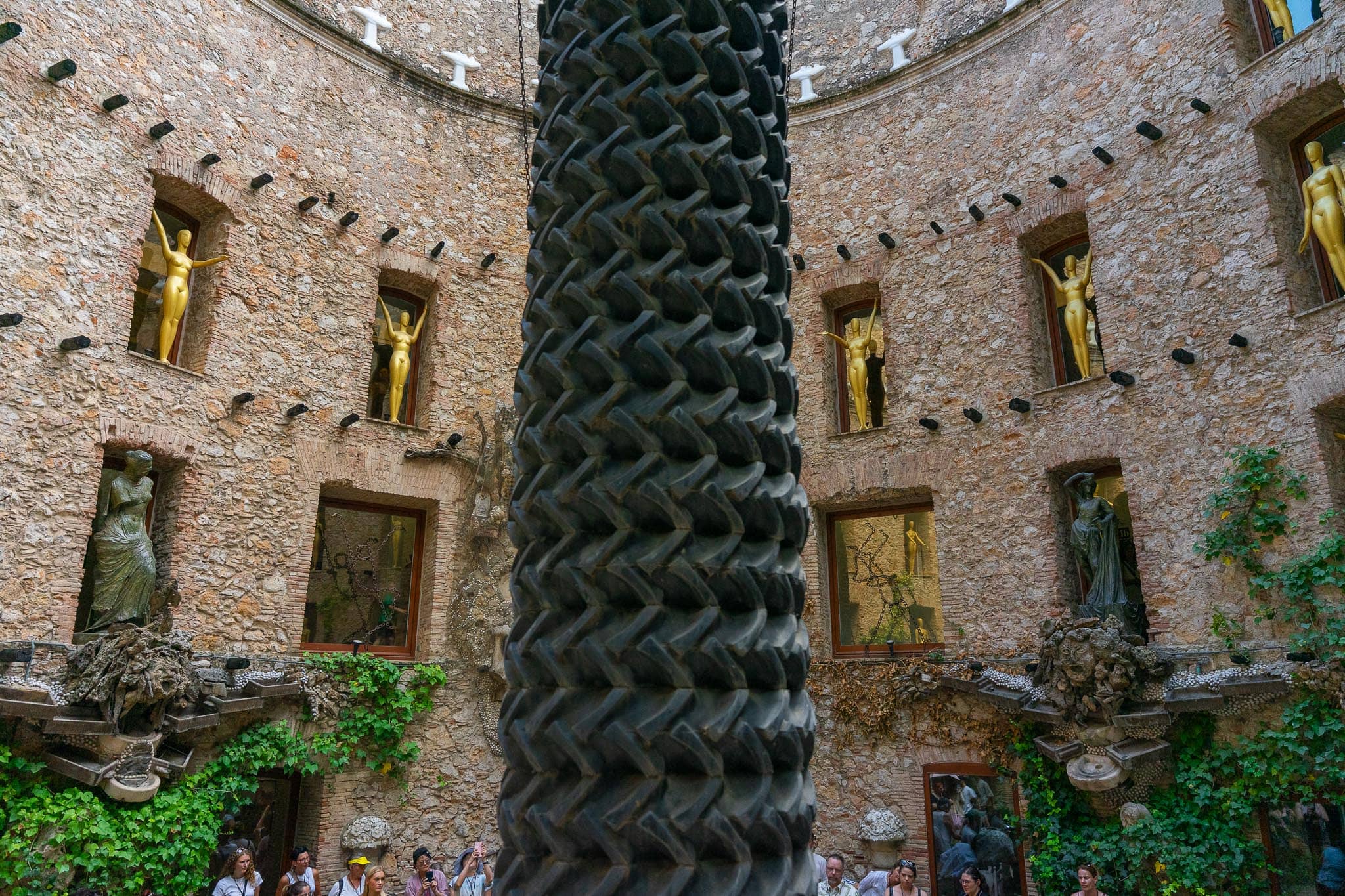 The courtyard of the Teatre-Museu Dali at Figueres, its stone walls lined with gilded figures in niches, a dark textured column at the centre and visitors below.