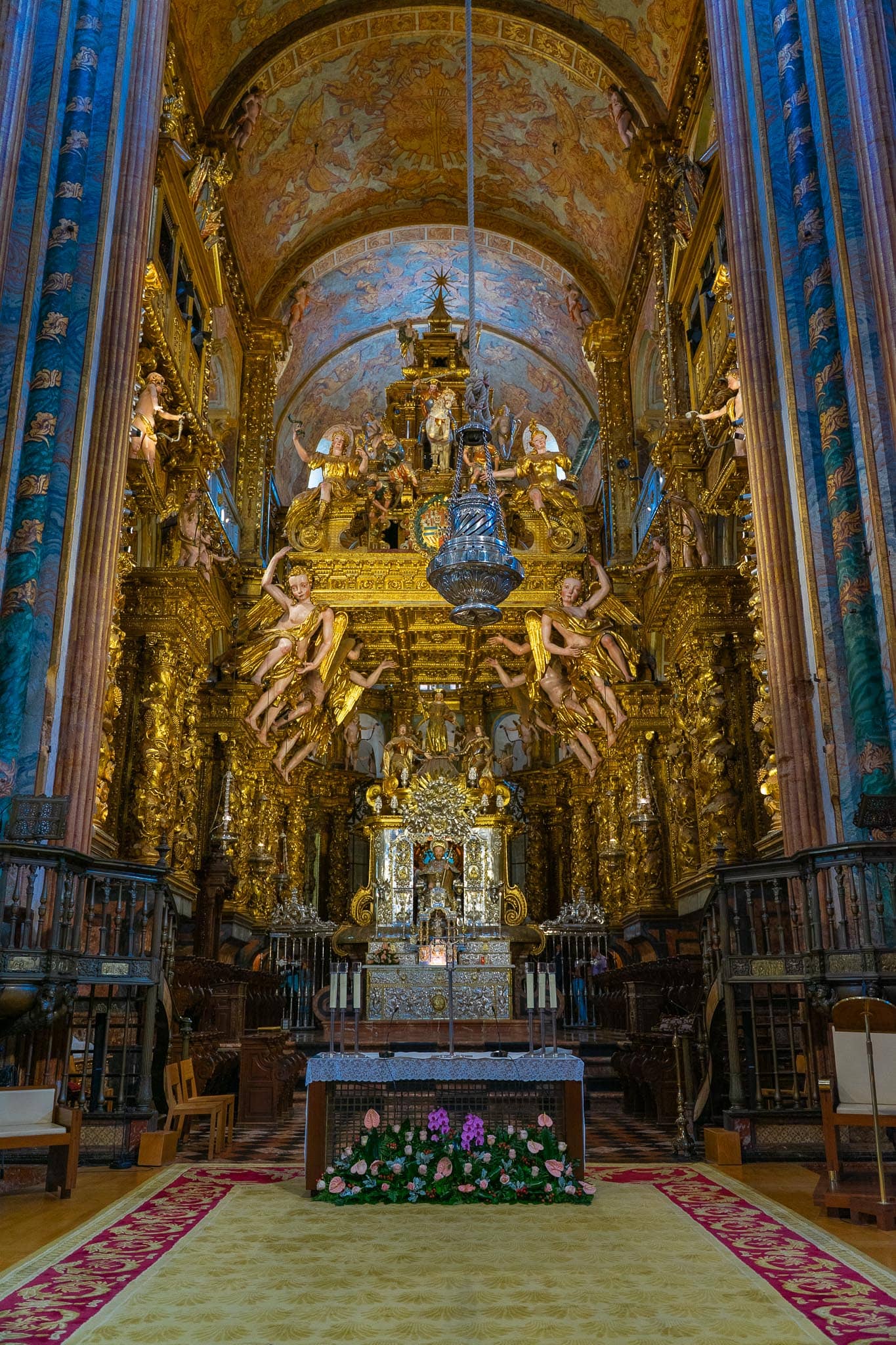 The gilded baroque high altar and baldachin of Santiago de Compostela cathedral, framed by blue-painted piers and a vaulted apse.