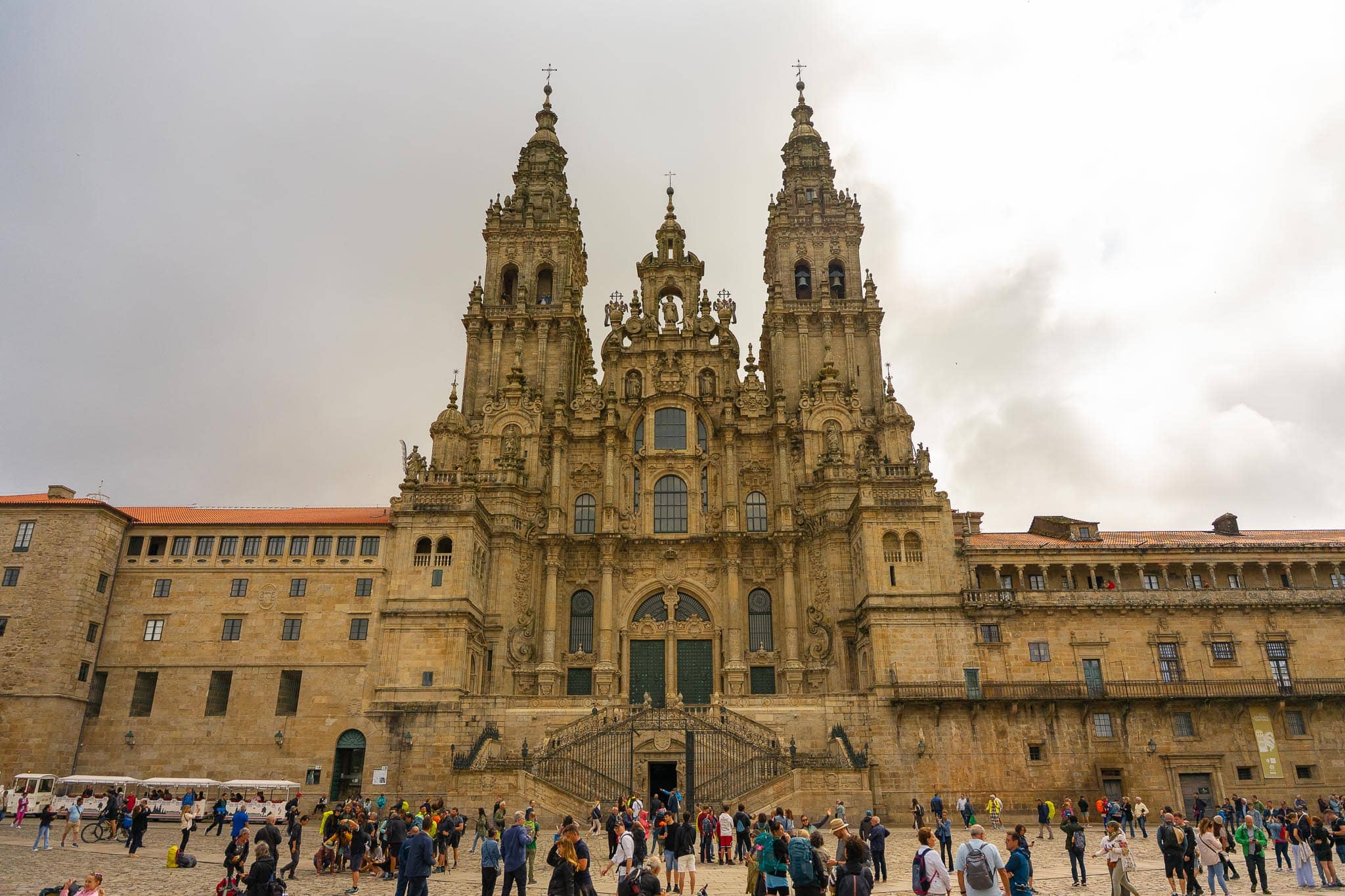 The baroque Obradoiro facade of Santiago de Compostela cathedral above its double staircase, with crowds gathered across the granite square below.