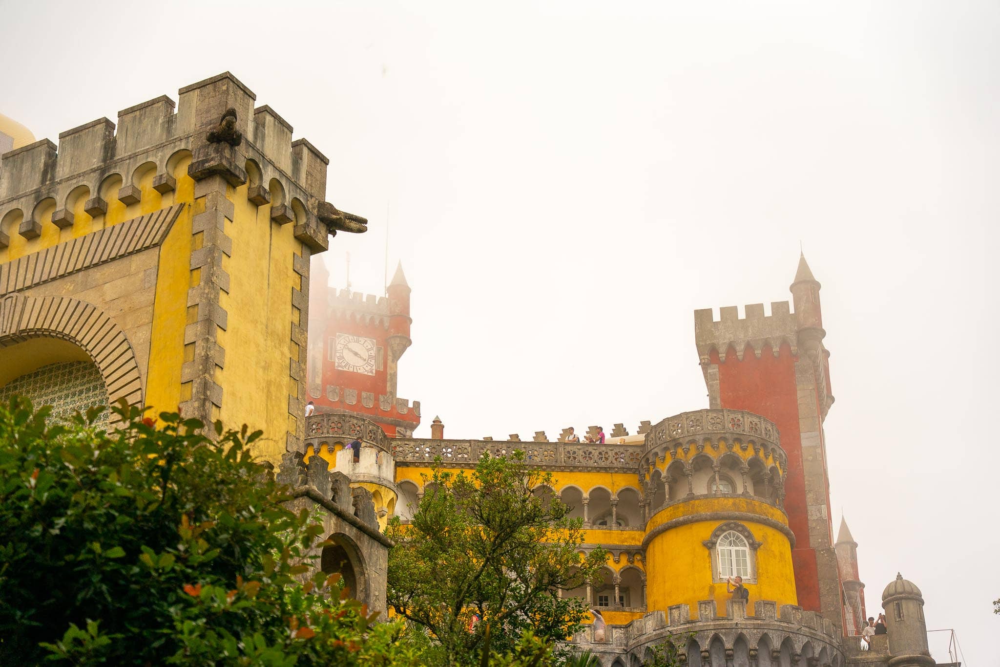 The yellow and red walls, crenellations and clock tower of the Pena Palace at Sintra, half dissolved in thick white mist.