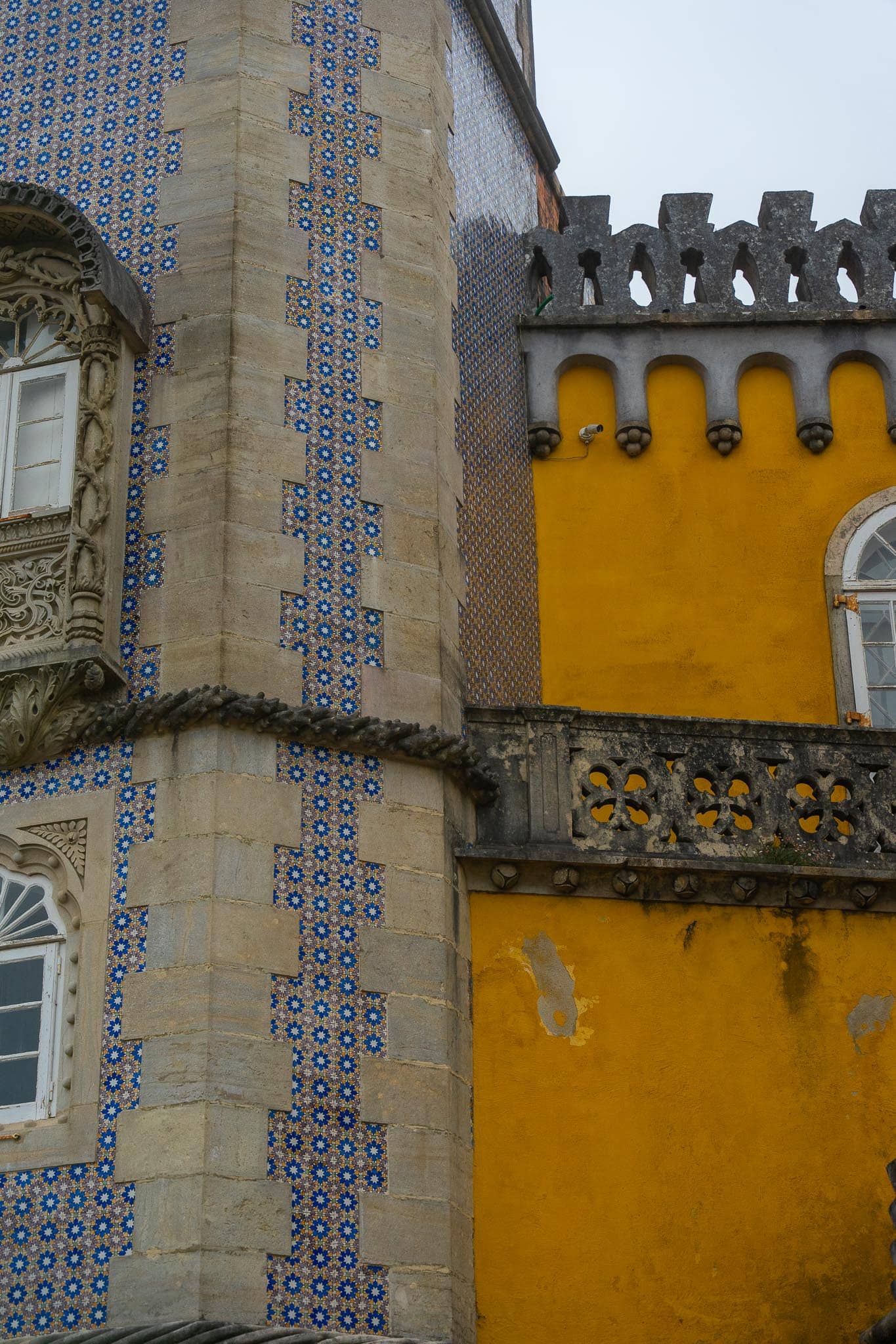 A detail of the Pena Palace at Sintra: a wall panelled in blue-and-white azulejos meeting a wall of flat ochre-yellow render under battlements.