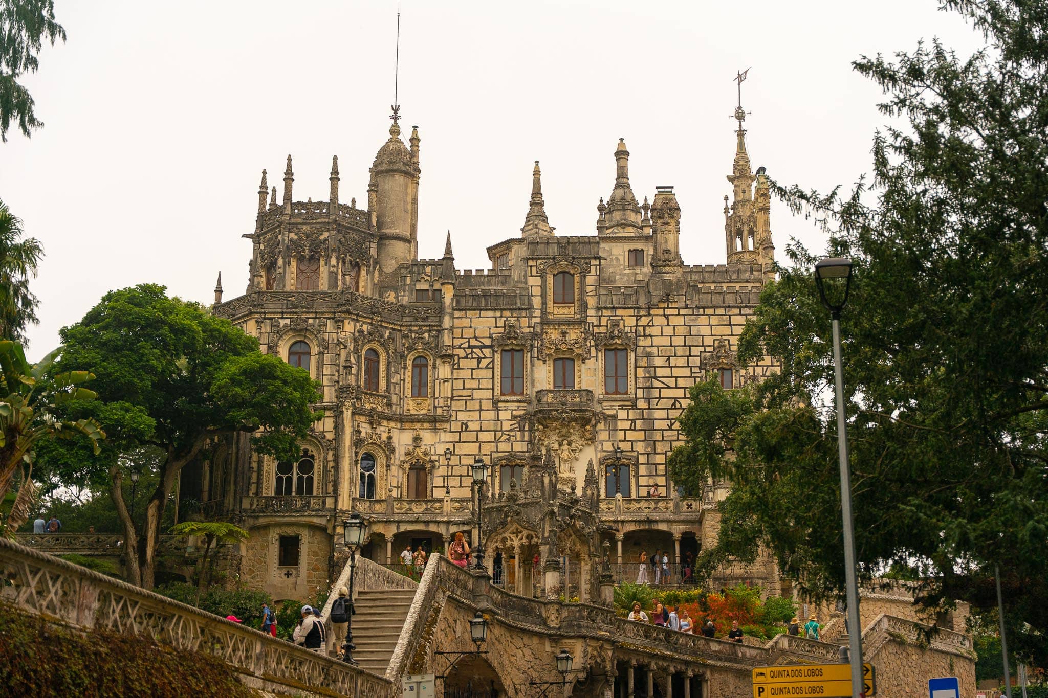The pinnacled neo-Gothic facade of the Quinta da Regaleira at Sintra rising above terraces and stairs, framed by dark trees.