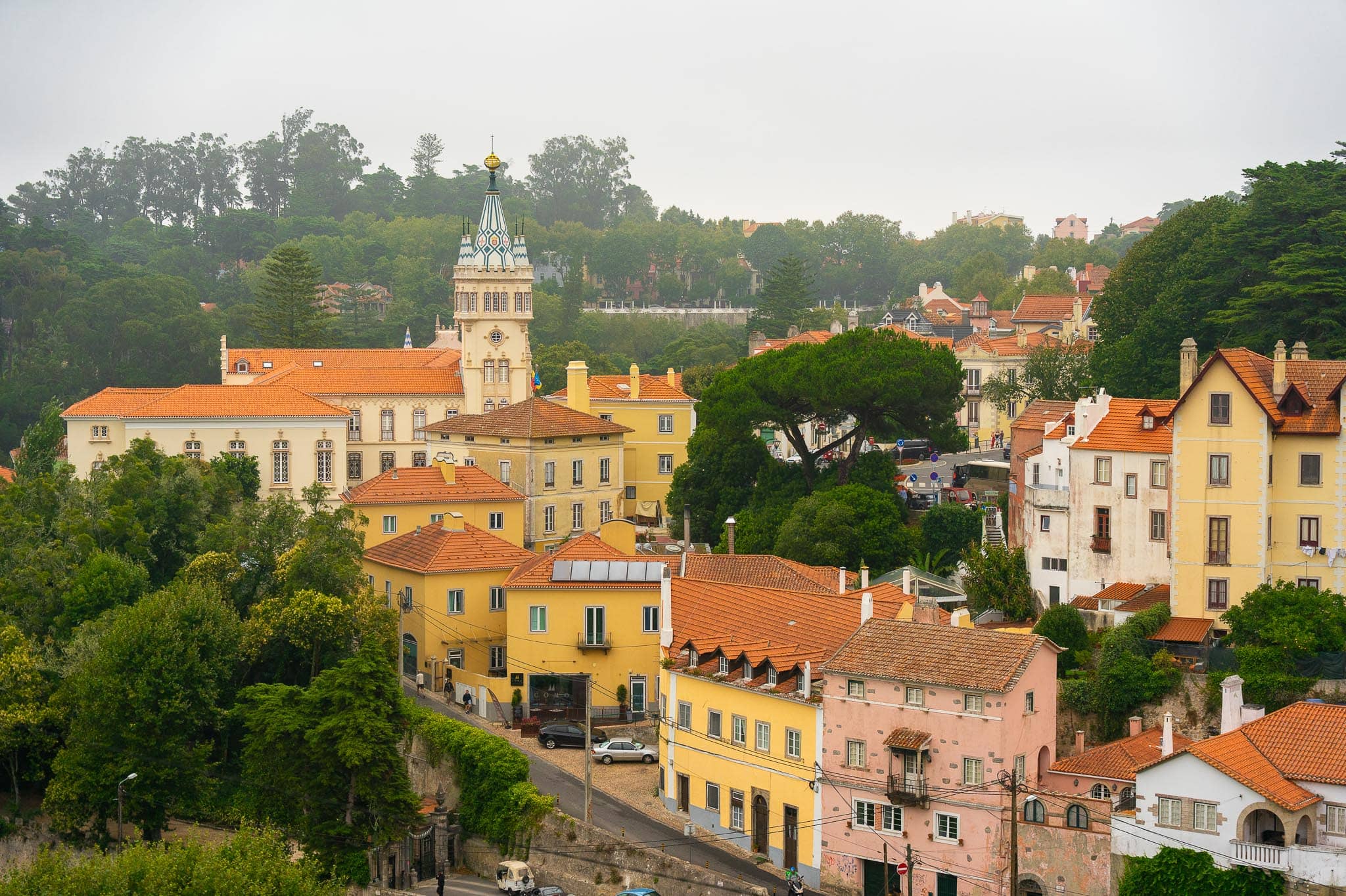 The pastel houses and terracotta roofs of Sintra town on a wooded slope, with the hillside above them disappearing into low mist.