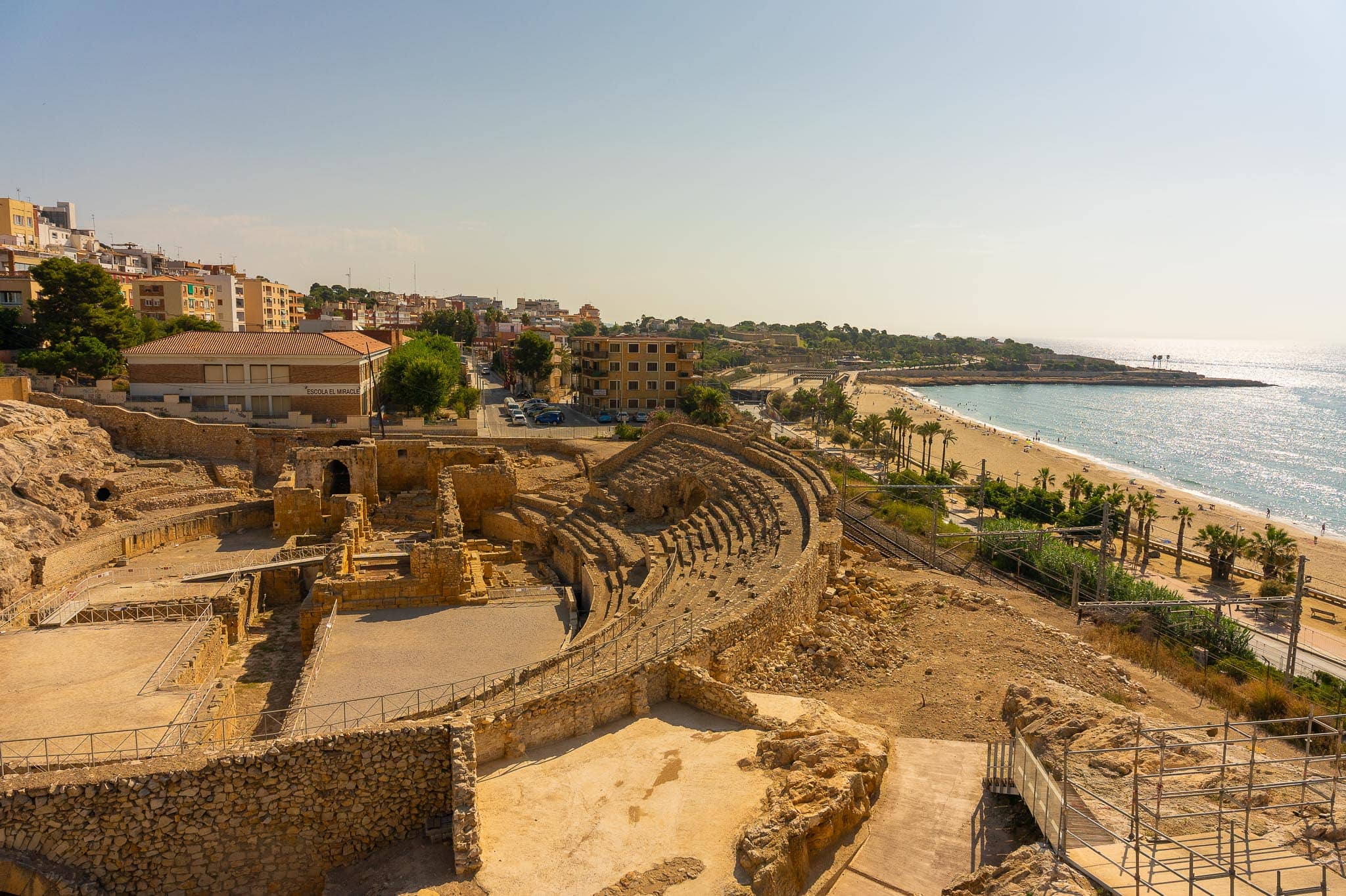 The stone tiers of the Roman amphitheatre at Tarragona cut into the hillside directly above a curving beach and the Mediterranean.