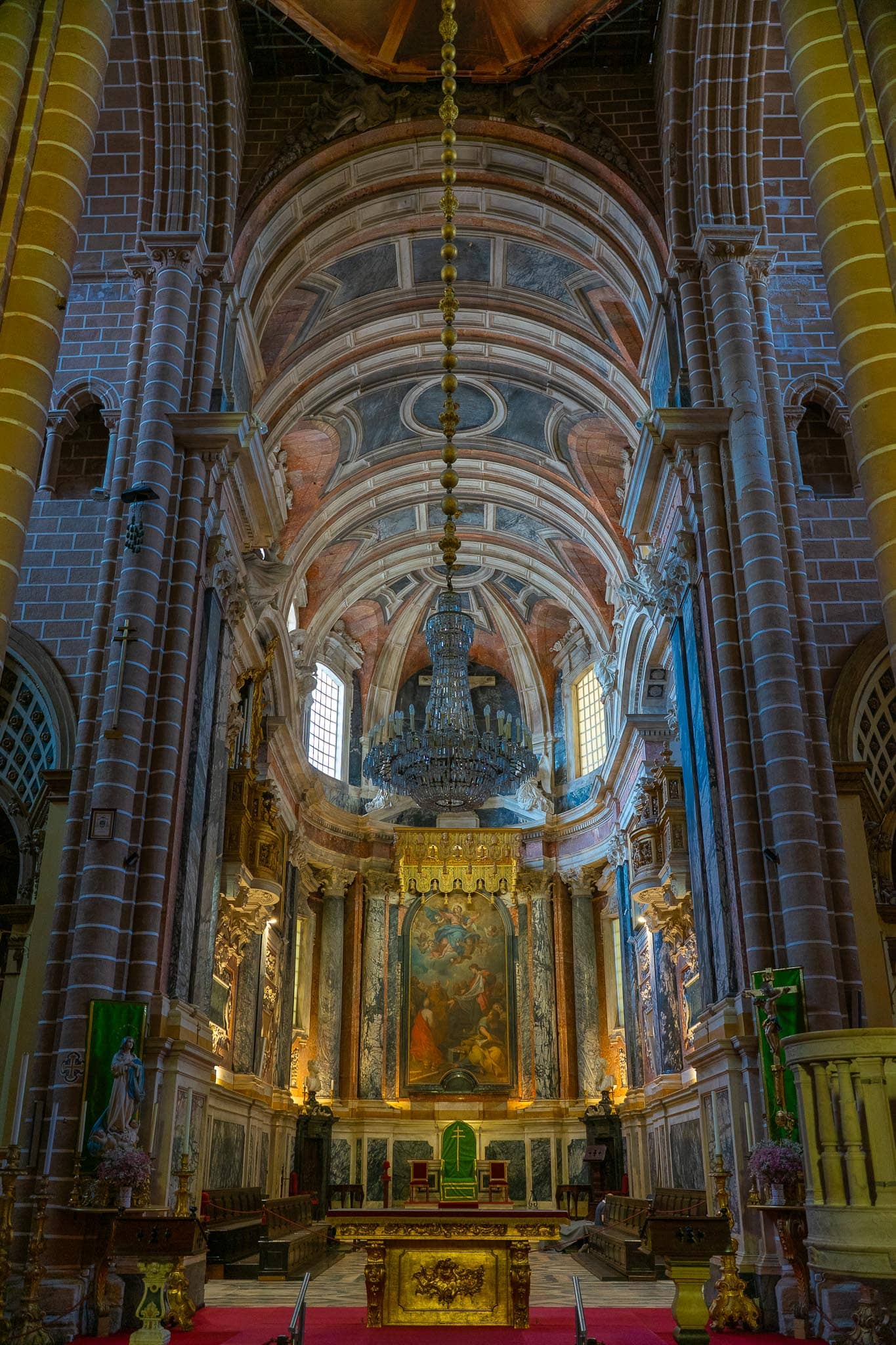 The nave of Evora cathedral looking towards a gilded baroque high altar, with ribbed Gothic vaulting and pale painted ceiling above.