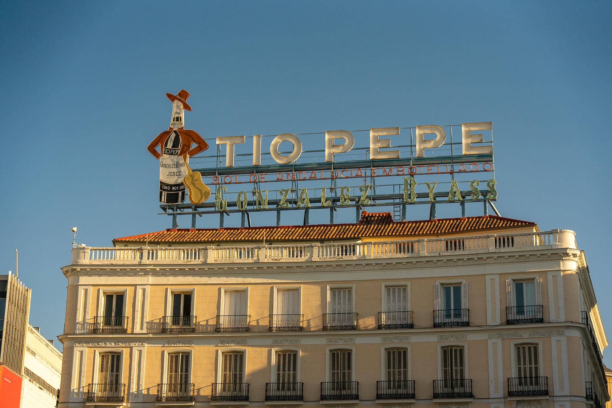 The Tio Pepe sherry sign, a bottle wearing a red hat and guitar, standing on the roofline of a pale building above the Puerta del Sol in Madrid.