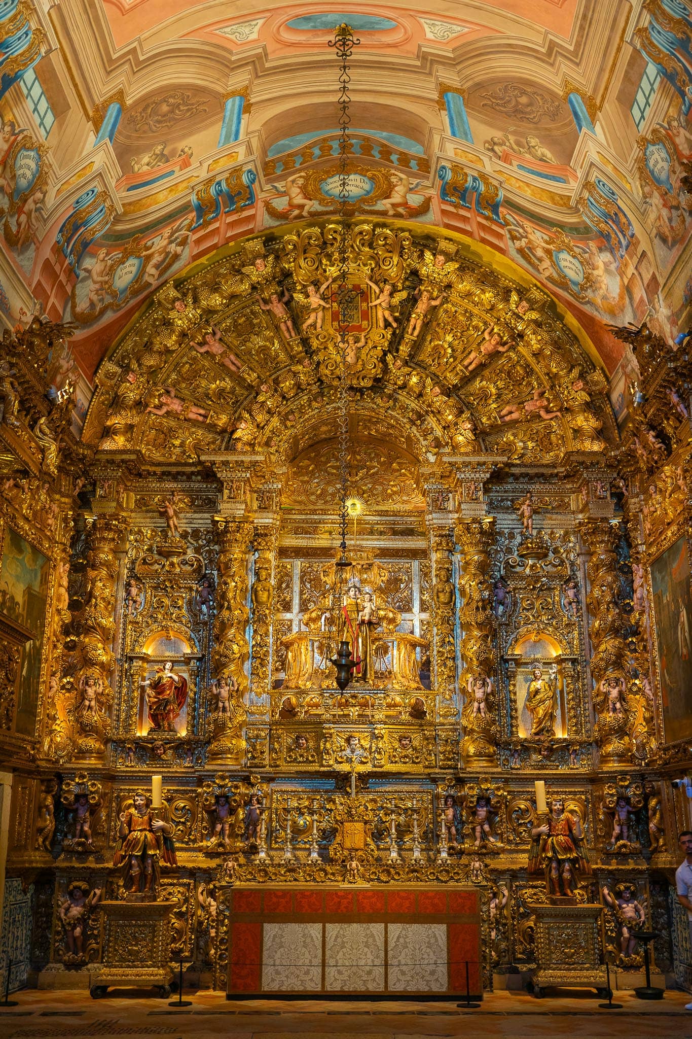 A baroque altarpiece of carved and gilded woodwork rising to painted vaulting, with gilded figures flanking the altar, in a church in Lagos.