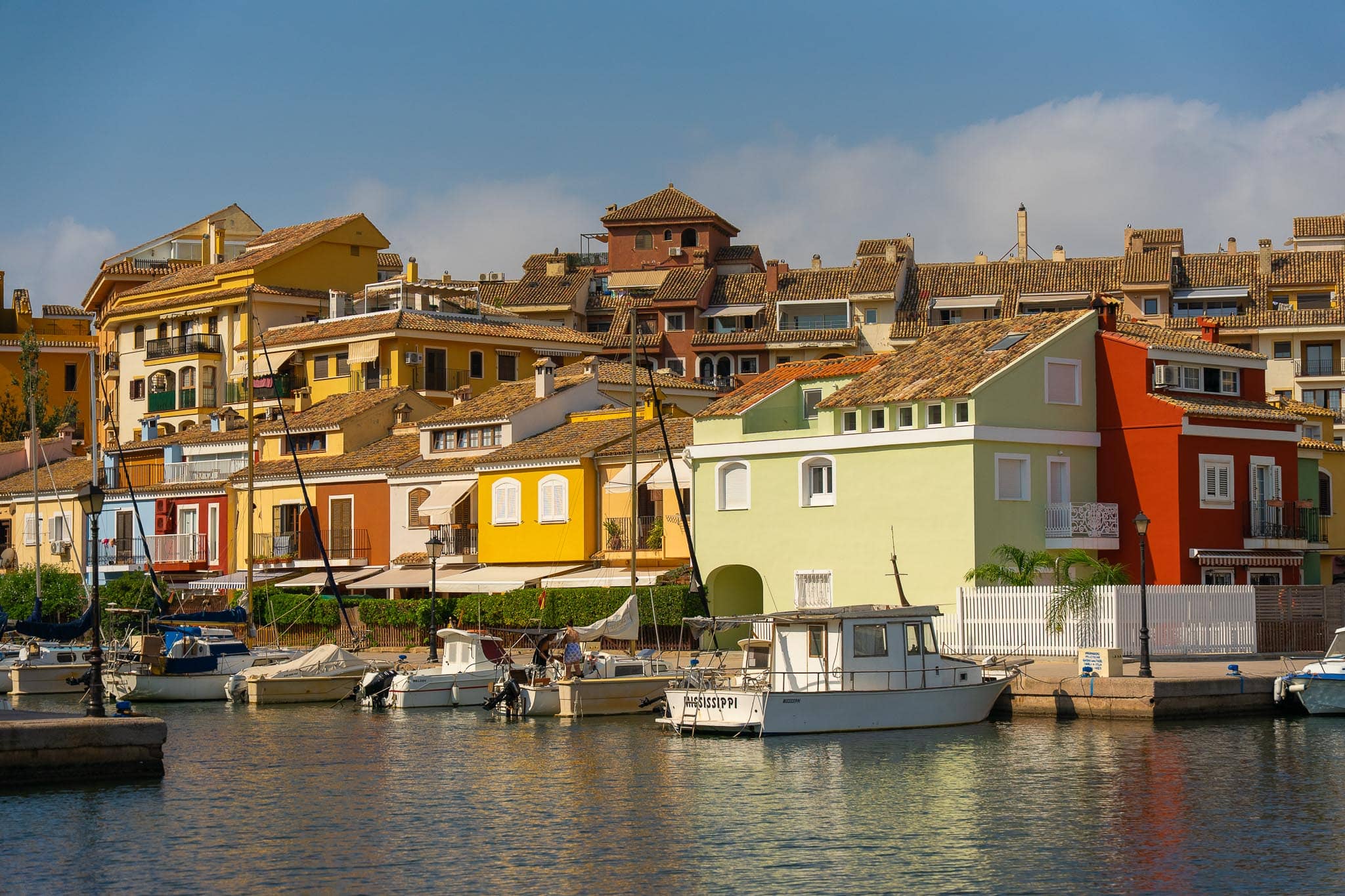 Brightly painted houses in red, yellow and green above a small harbour of moored fishing and pleasure boats near Valencia.