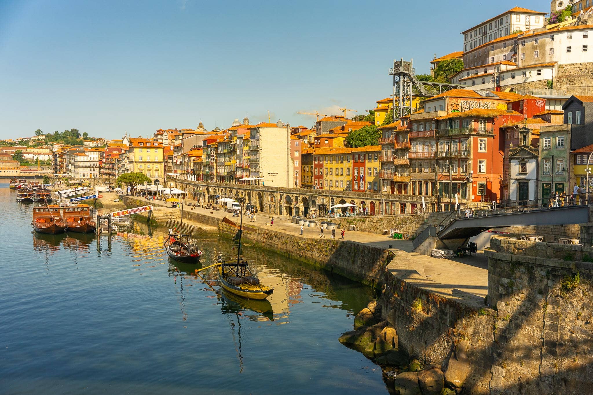 The Ribeira waterfront in Porto: tall narrow houses in ochre and white above a stone quay, with flat-bottomed rabelo boats moored on the Douro.