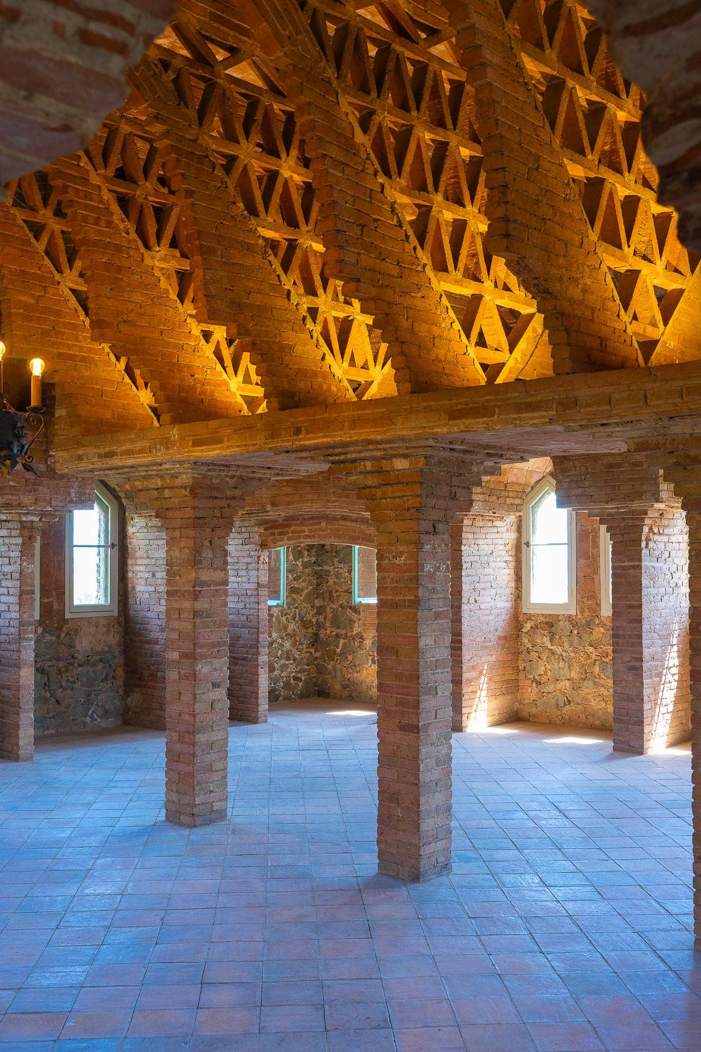 The attic of Torre Bellesguard in Barcelona: brick piers supporting a ceiling of stepped brick arches lit warm from below, above a tiled floor.