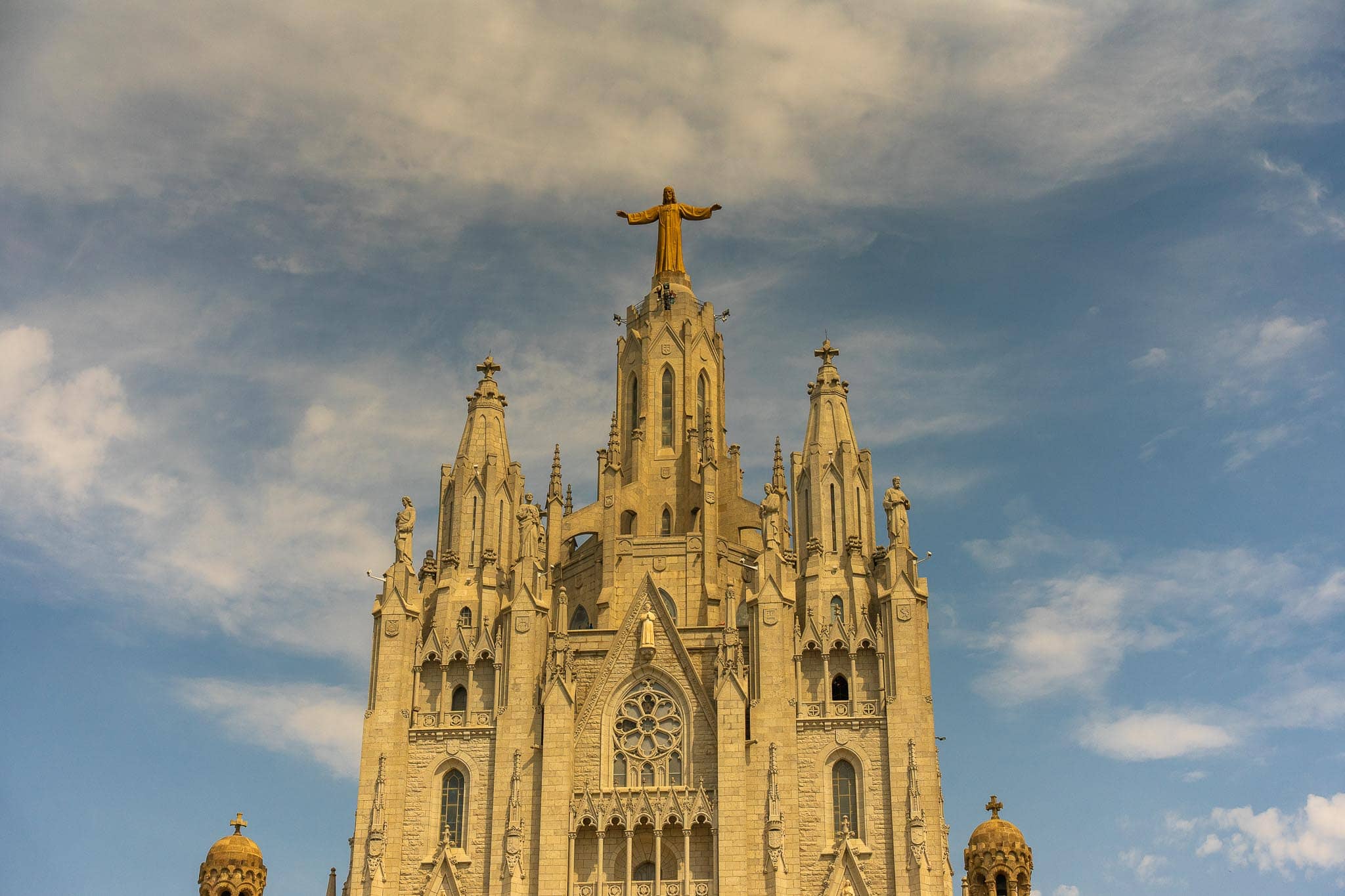 The pale stone towers of the Temple Expiatori del Sagrat Cor on Tibidabo, topped by a bronze figure of Christ with arms outstretched against cloud.