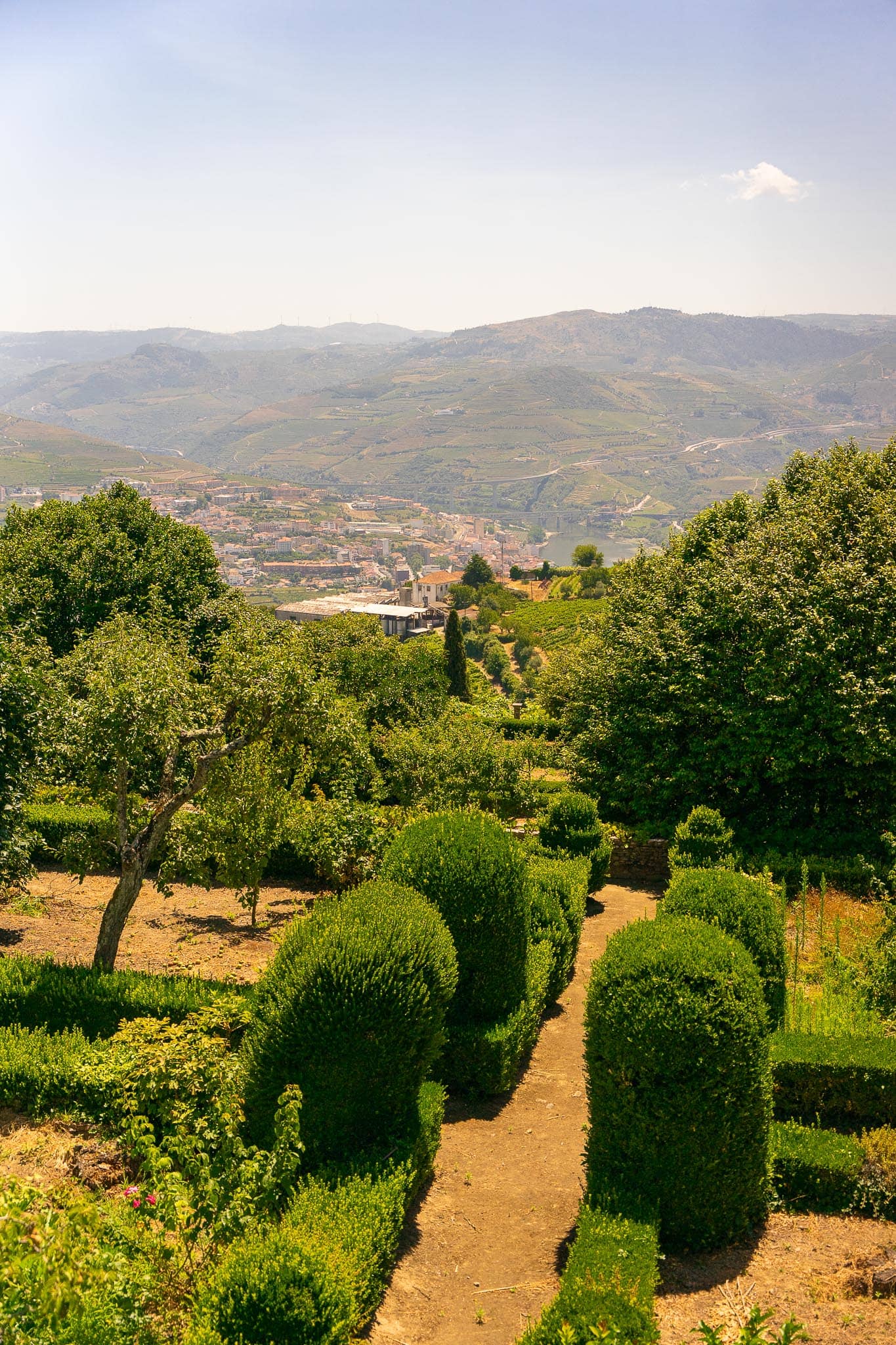 A formal garden of clipped box hedges and gravel paths at a Douro valley quinta, looking out over the wooded valley and hills beyond.