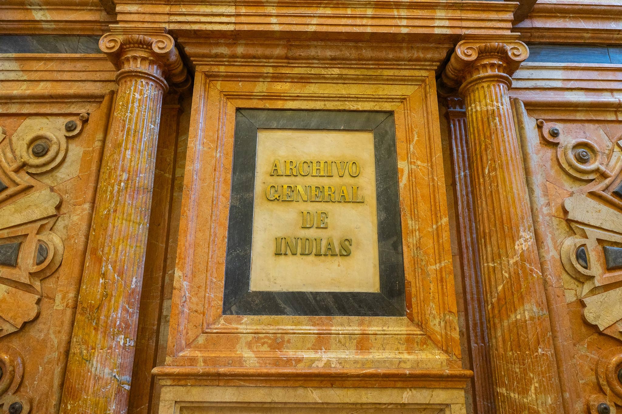 The words ARCHIVO GENERAL DE INDIAS in gilded raised letters on a pale marble tablet, framed by a dark marble surround and two fluted orange-veined marble columns.