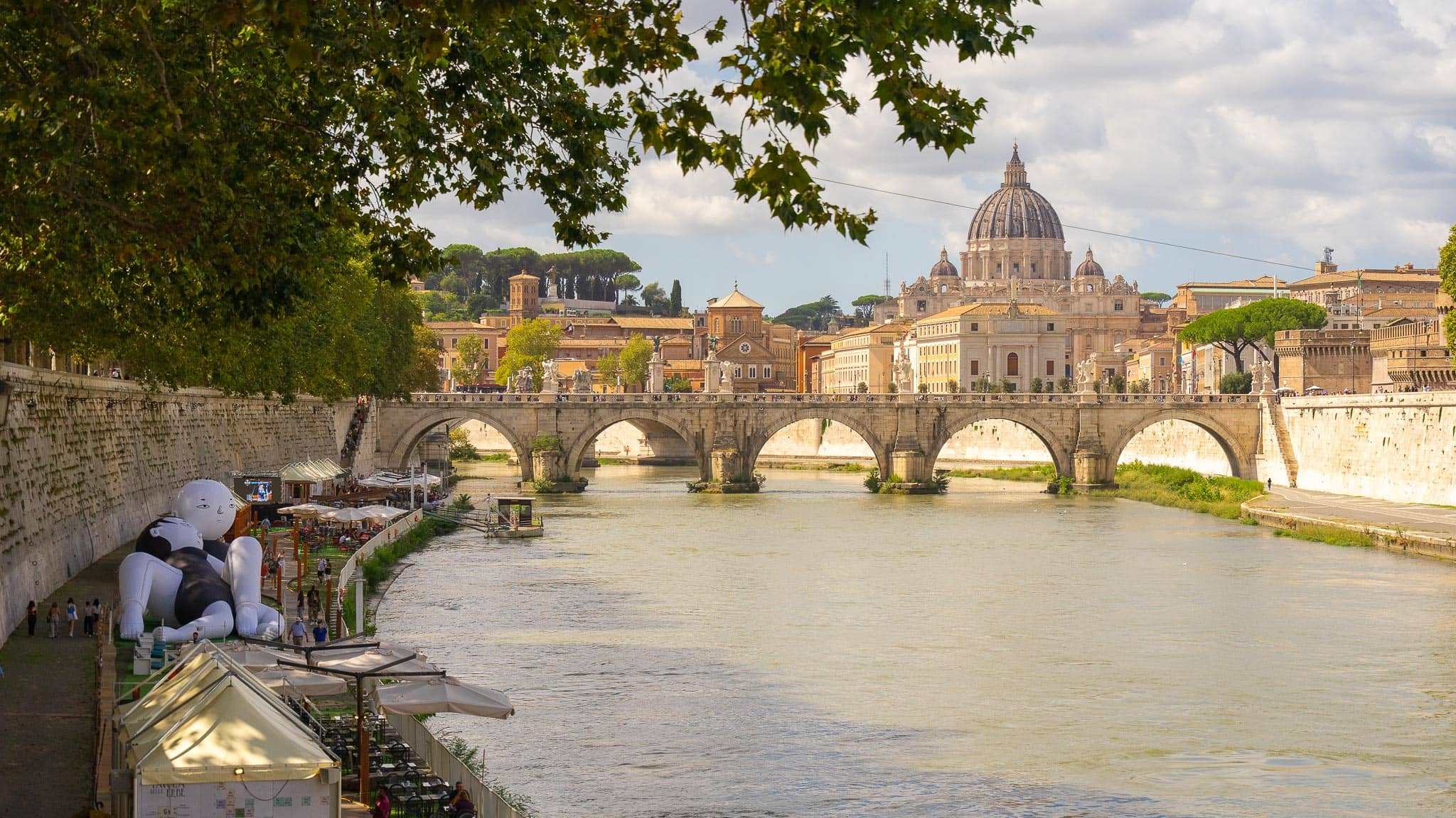The Tiber running between stone embankments towards the arches of the Ponte Sant'Angelo, with the dome of St Peter's Basilica on the skyline beyond.
