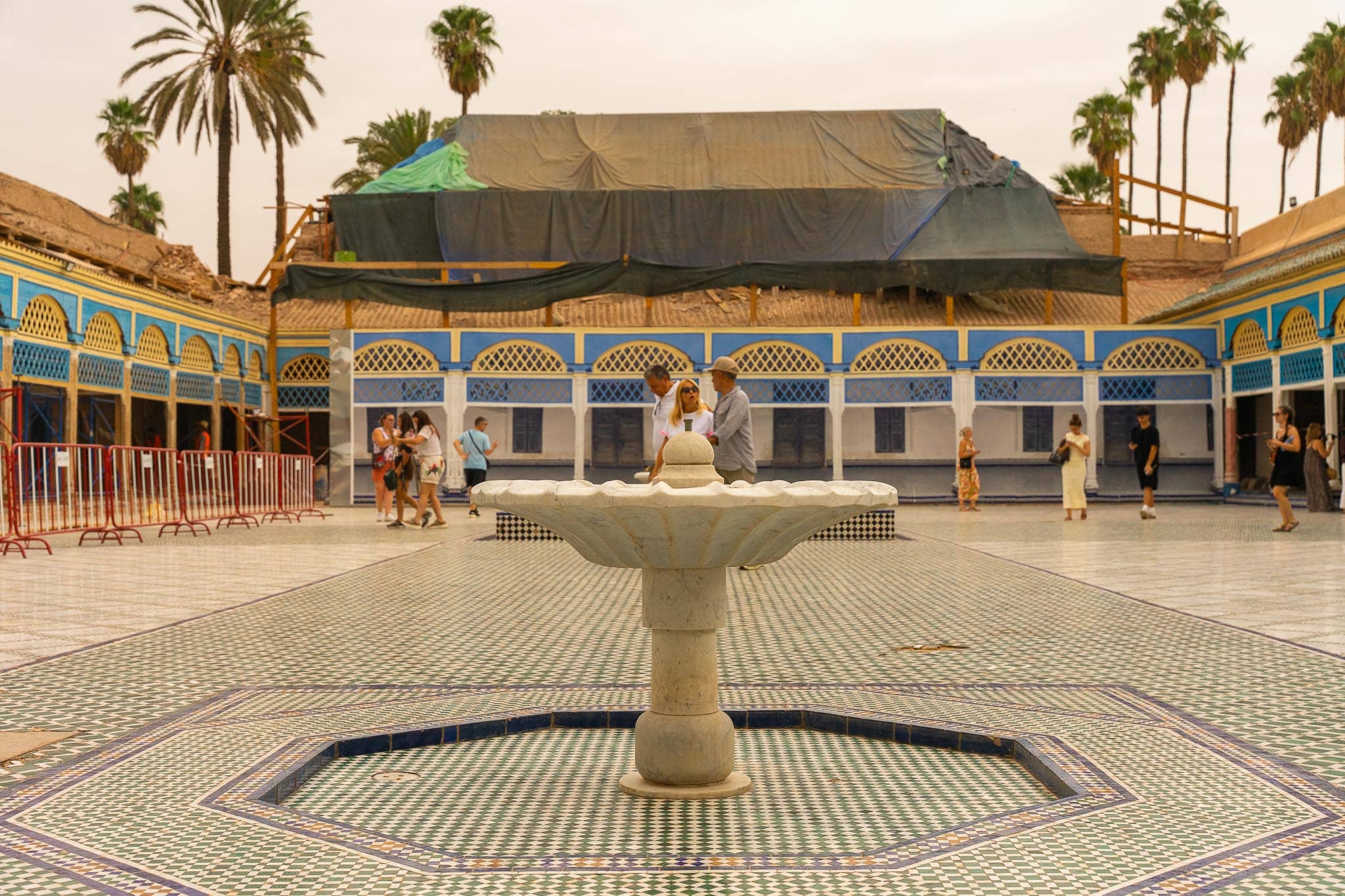 A large tiled courtyard at the Bahia Palace in Marrakech with a central marble fountain, blue-and-white painted arcading on all sides and palms above the roofline.